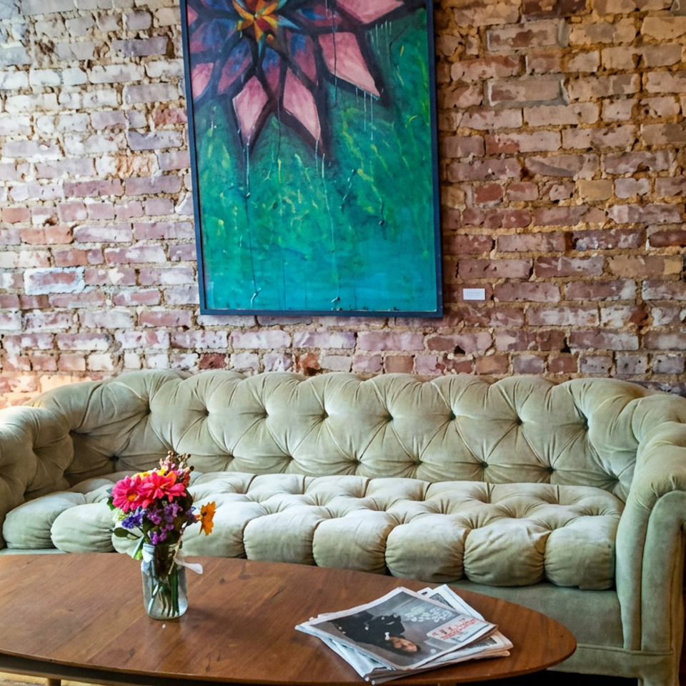 Cozy restaurant lounge with a tufted mint-green sofa, flower vase, coffee table, exposed brick wall, and colorful artwork.