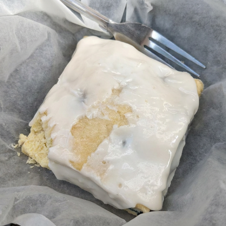 Rectangular iced pastry served on parchment paper in a basket, with a fork resting above it.